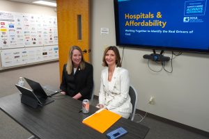 Laura Appel and Shannon Striebich sit in front of a Hospitals & Affordability presentation slide. 